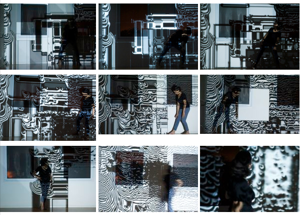 Person standing or walking in front of a wall covered with abstract, circuitry-like black-and-white patterns.