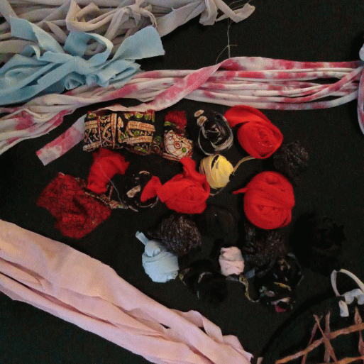Assorted fabric scraps, ribbons, and yarns in pinks, blues, and reds scattered on a dark surface.